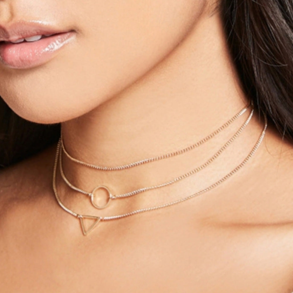 The stylish Kelabu geometric statement necklace in gold being worn by a woman with long brown hair and shiny, glossy lips