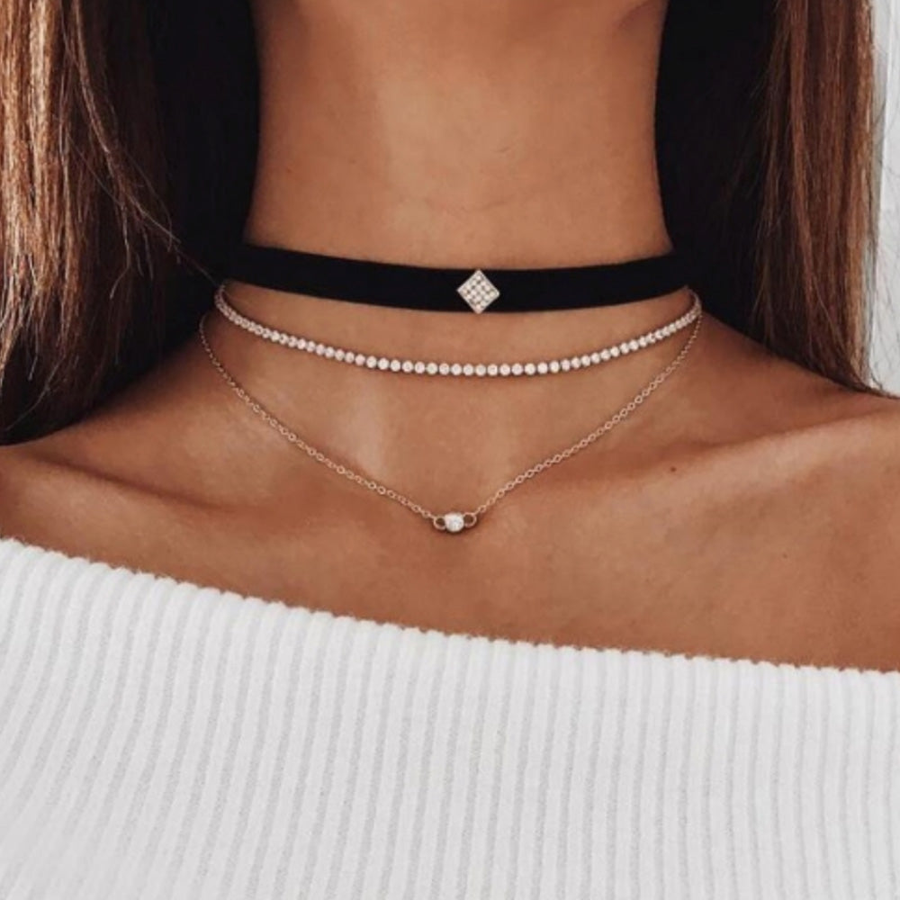 The stylish layered choker from Kelabu, with velvet, gold and crystal designs, being worn by a woman with long brown hair and wearing an off the shoulder white jumper