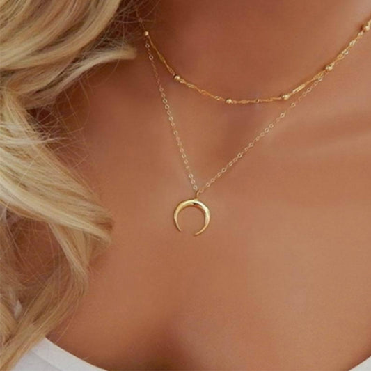 The Kelabu gold horn necklace being styled by a woman with long blonde hair and wearing a white t-shirt