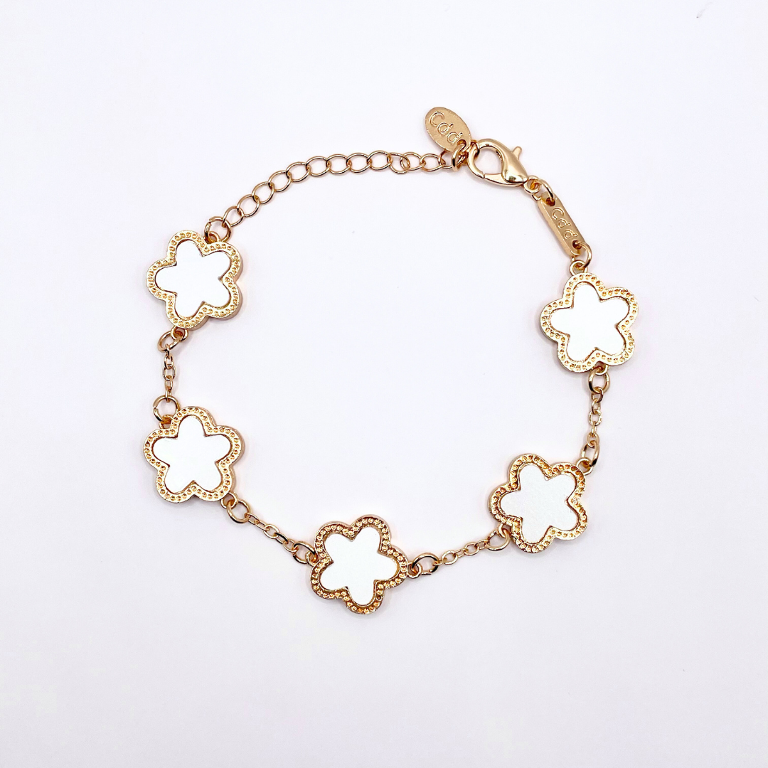dainty gold bracelet with clover flower charm detailing on white background