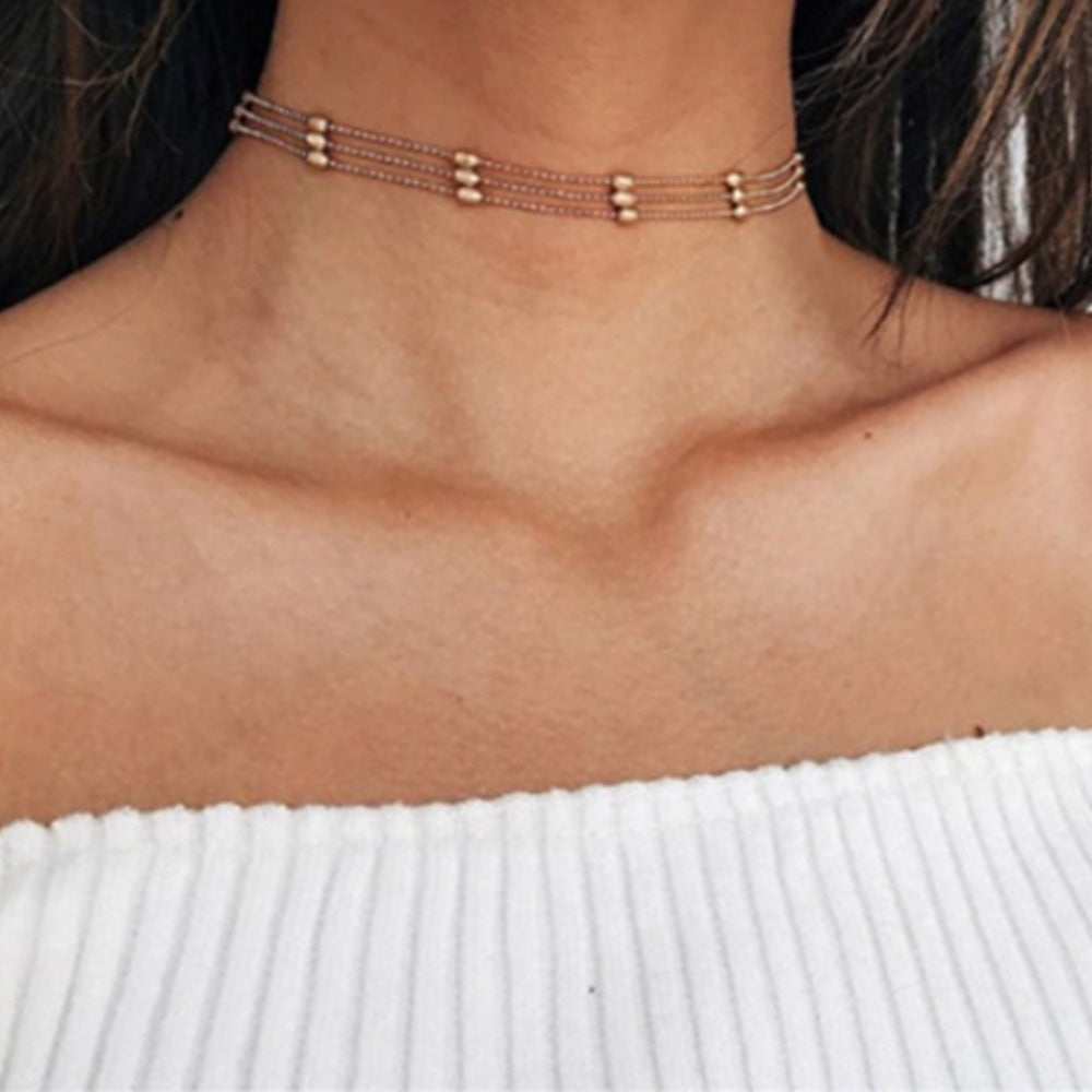 Woman with dark hair wearing gold boho choker and an off the shoulder jumper 