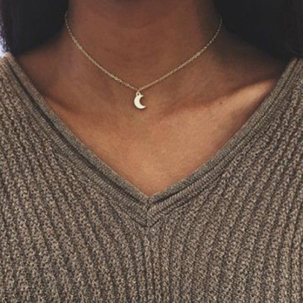 Woman wearing the dainty moon pendant necklace in Gold with a v-cut khaki coloured chunky knit jumper