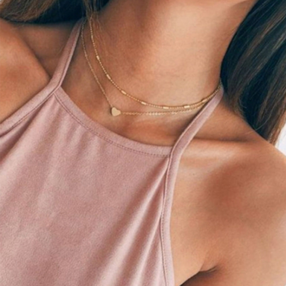 Woman wearing the stylish heart charm necklace and choker set in gold from Kelabu with a dusty pink high neck vest top on 