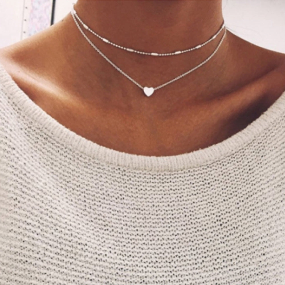 Woman wearing the silver heart charm necklace set with a cream jumper on 