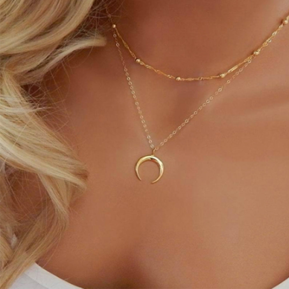 The Kelabu gold horn necklace being styled by a woman with long blonde hair and wearing a white t-shirt 